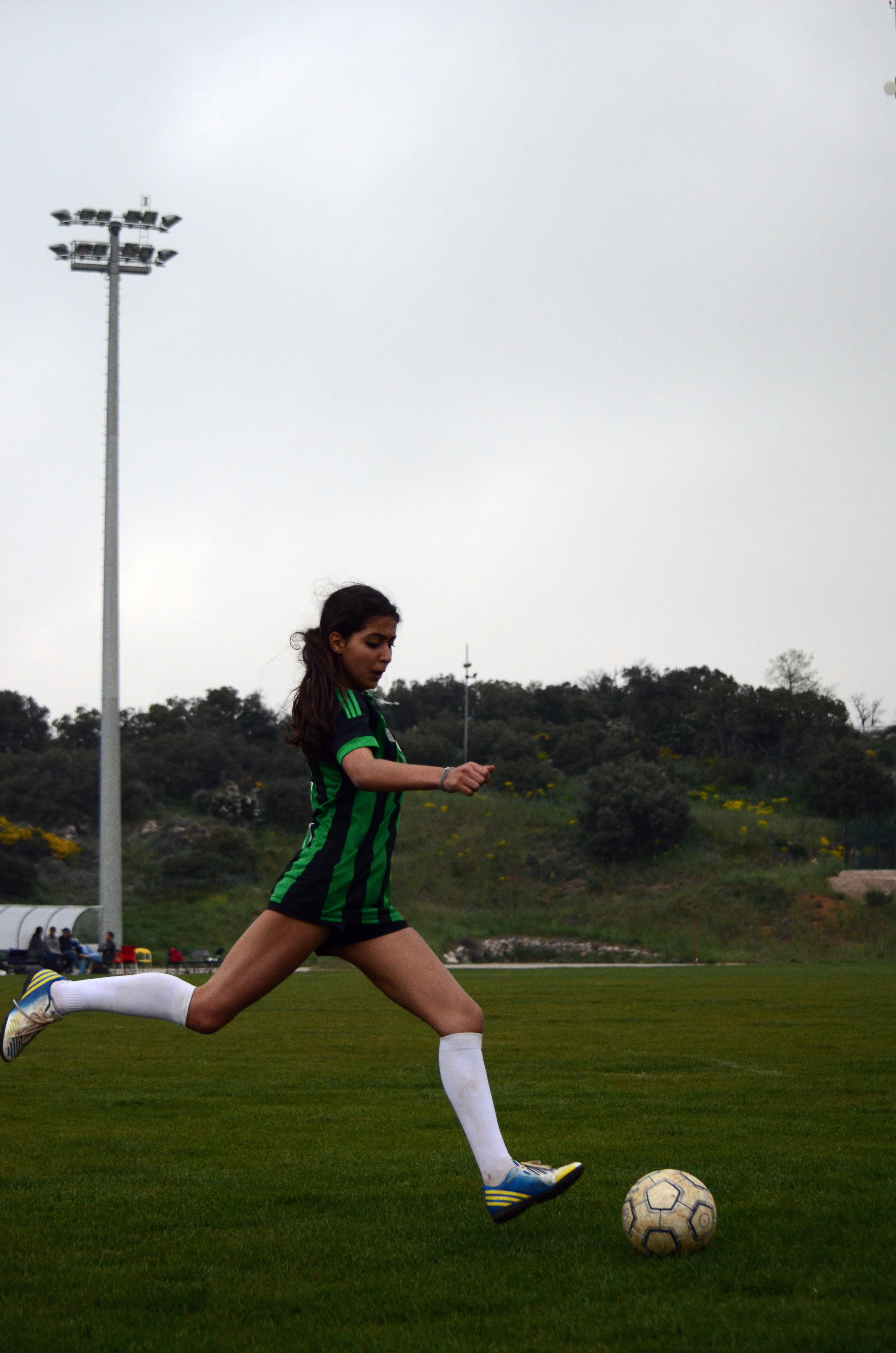 A young woman in a black and green jersey making a dynamic play at a soccer game.