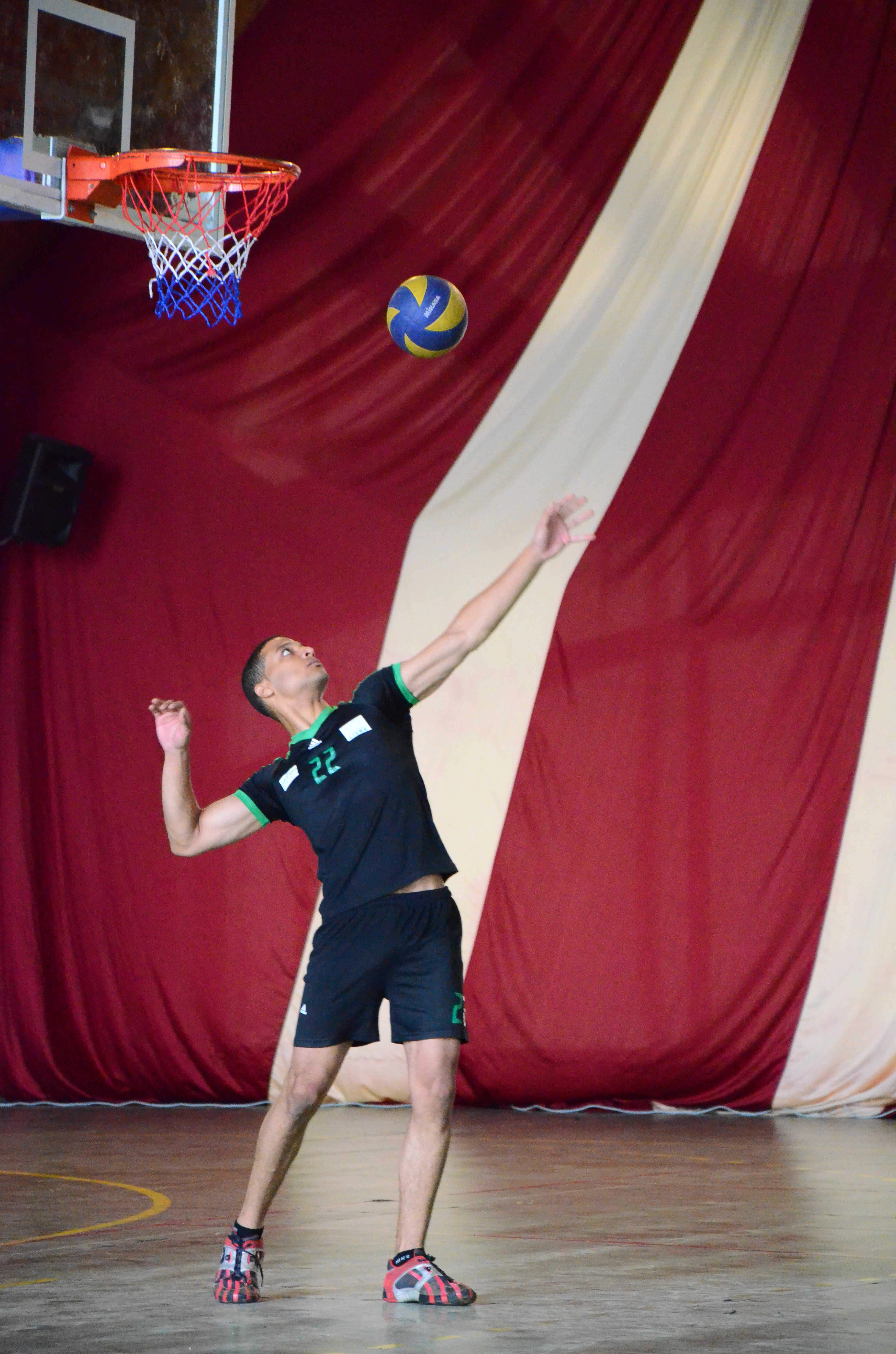 A young man in a black jersey with the number 22 on his chest gets ready to serve at a volleyball game.